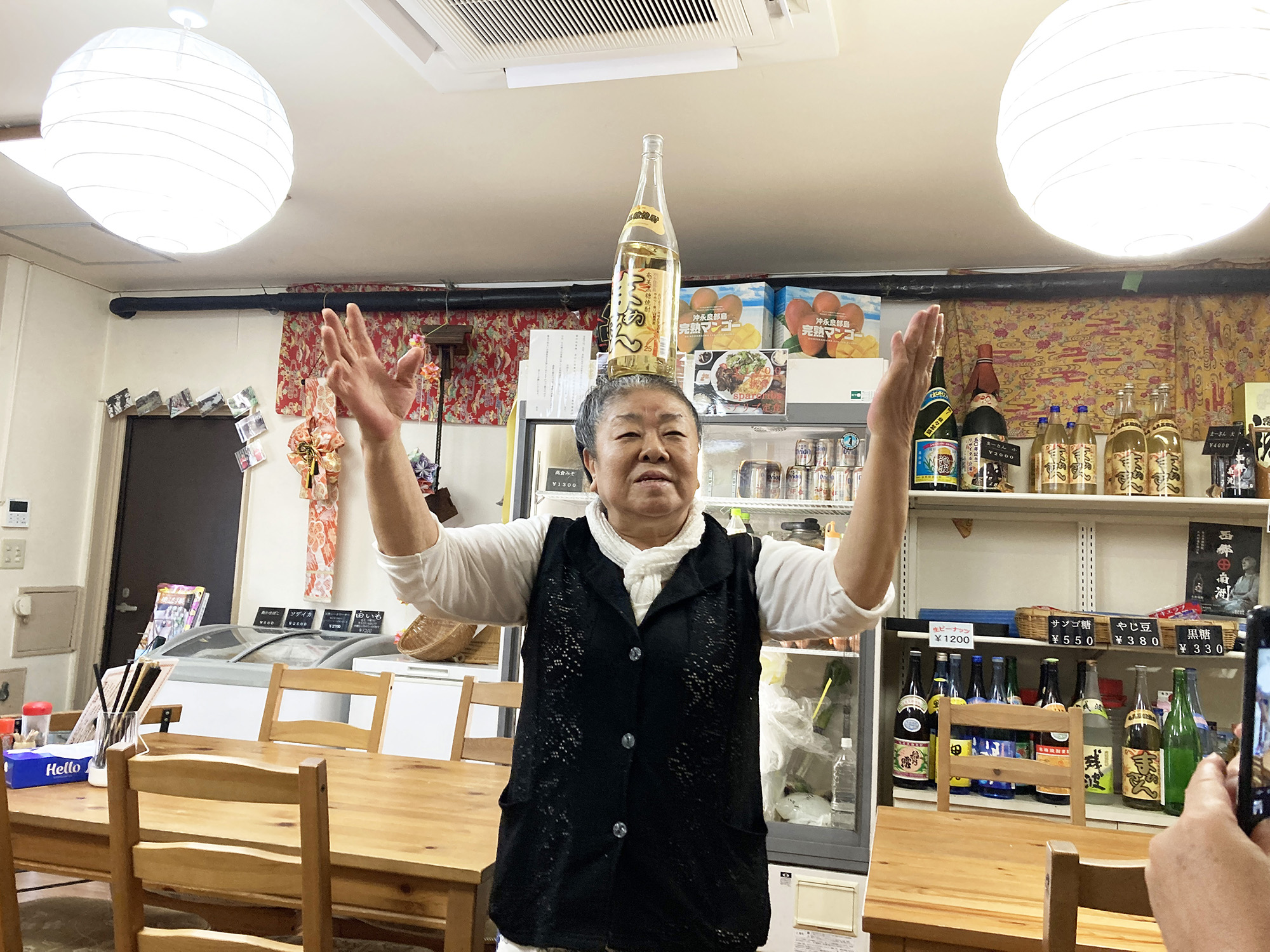 黒糖焼酎「まぁさん」の瓶を頭に乗せて踊っている「南国キッチン次郎」店主の森君枝さん。