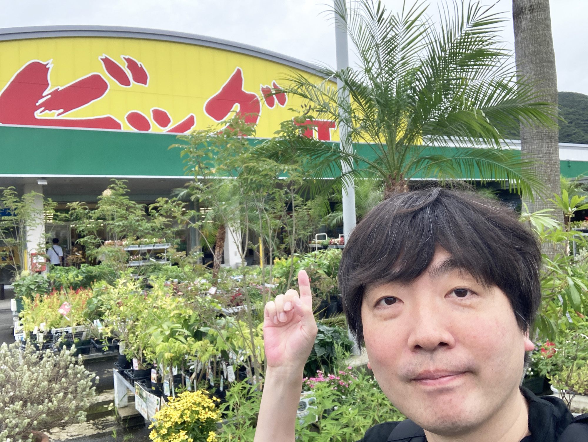 「ビッグツー」の外観を奥にしたスズキナオさんの自撮り写真。