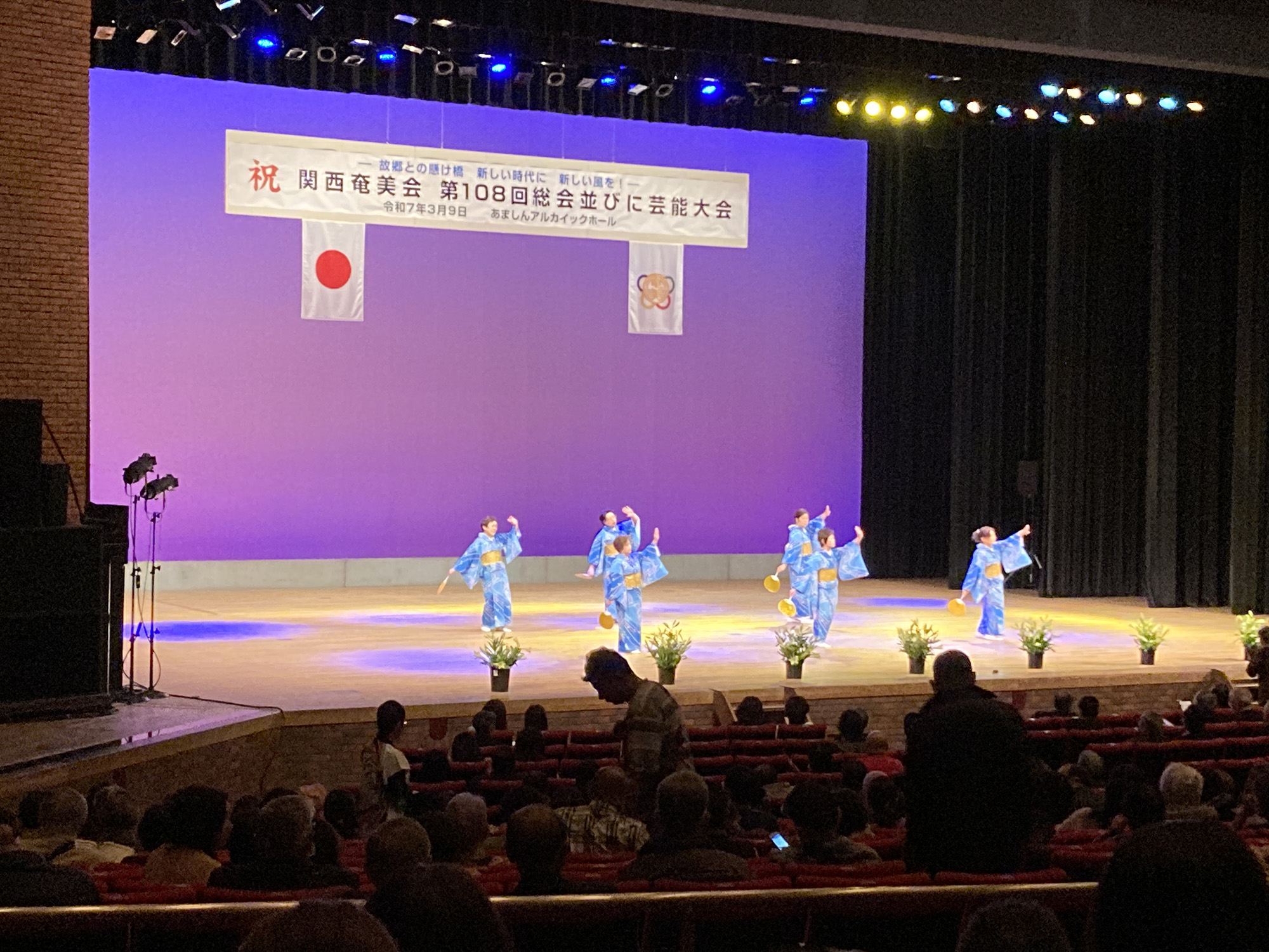 「関西奄美会 第108回総会並びに芸能大会」での近畿笠利会のステージの様子の写真。